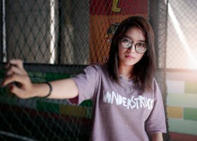 Portrait of a young woman wearing eyeglasses and a 'Wonderstruck' t-shirt posing indoors.